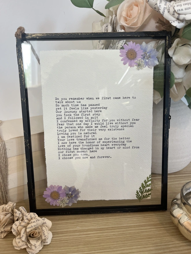 Framed typewriter print hand typed with an antique typewriter onto cotton rag handmade deckled paper. It is displayed in a black hanging rustic frame with gold brush detailing and decorated with real pressed dried flowers.