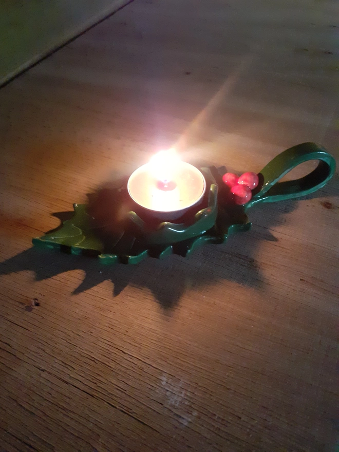 Festive green holly leaf tealight holder with red ceramic berries and glossy glaze, photographed in warm candlelight.