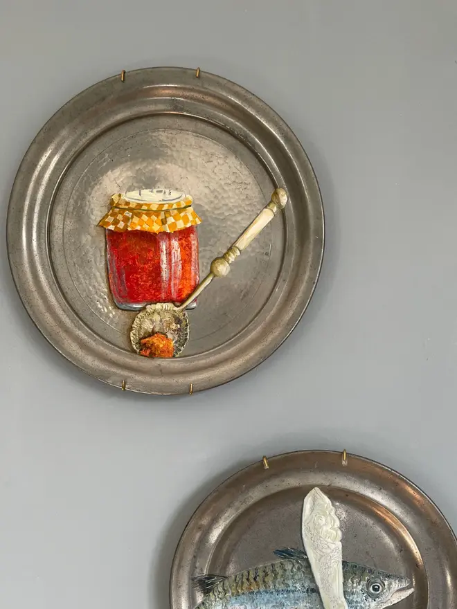 plate-scape. Oil Painted Spoon & Marmalade On Antique Pewter Plate hanging on a grey wall. 