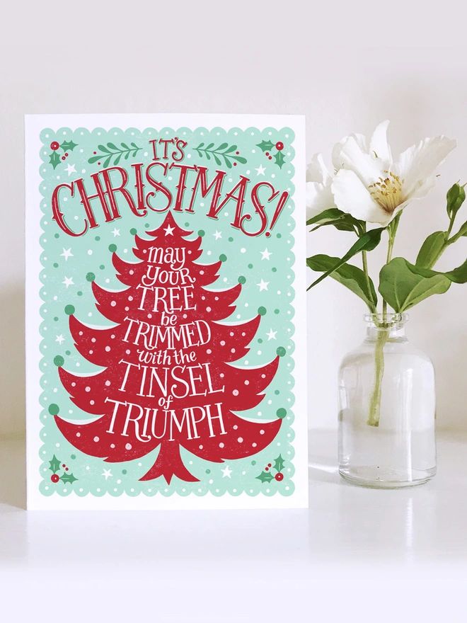 red and green christmas tree card with white flower in glass vase