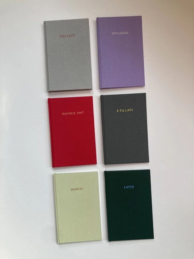 An array of handmade pocket sized notebooks in a variety of book cloth colours with personalised foiled quotes and titles