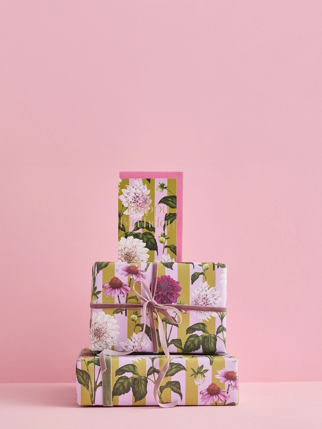 happy birthday card with gold foil wording and illustrated Dahlia flower on a green and pink stripes standing on a matching gift wrap tower