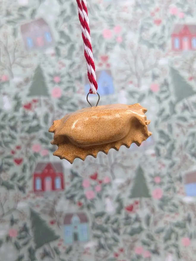 ceramic agnolotti christmas decoration. a small ceramic pasta decoration hanging from red and white thread.