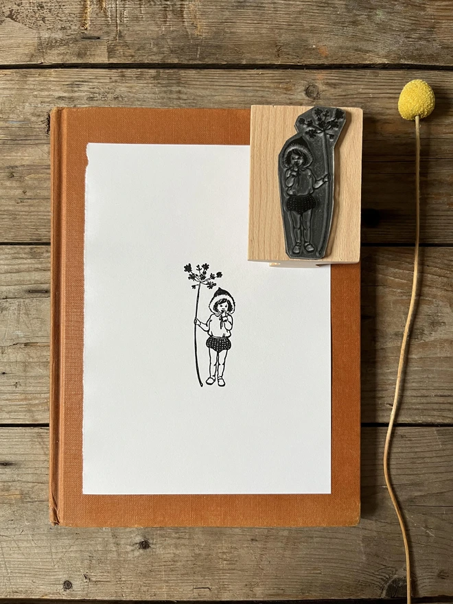 A christmas pixie holding a pretty twig stamped printed in black on a piece of white paper next to it is the original rubber stamp