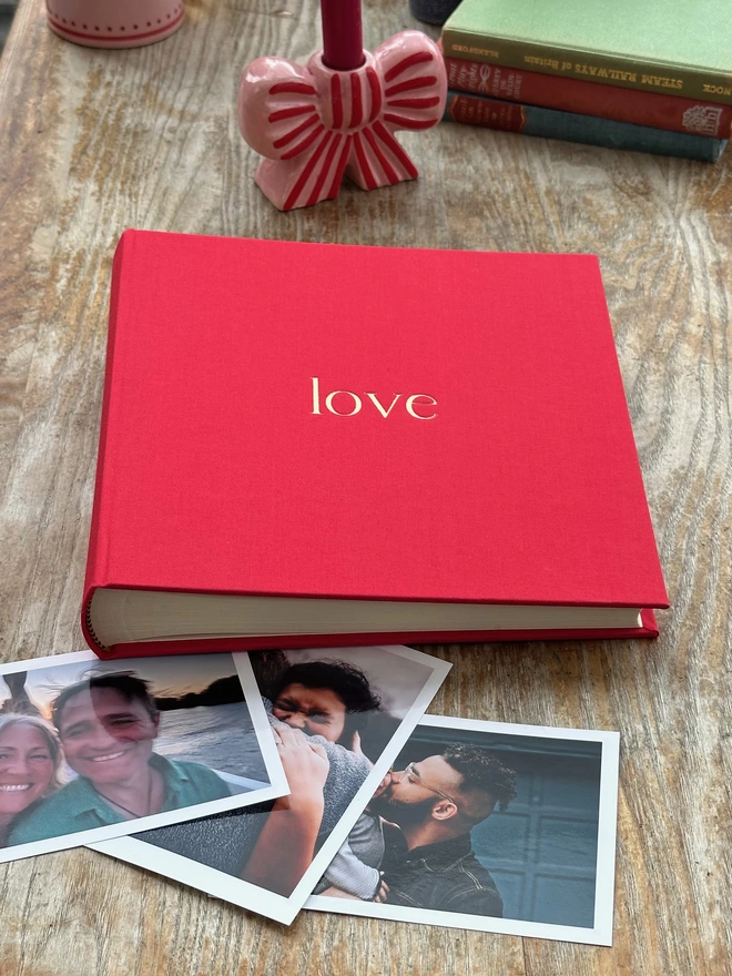 a red photo album has been printed with the word 'love' on the front in gold letters. On the table there are also lots of photos of friends and family.