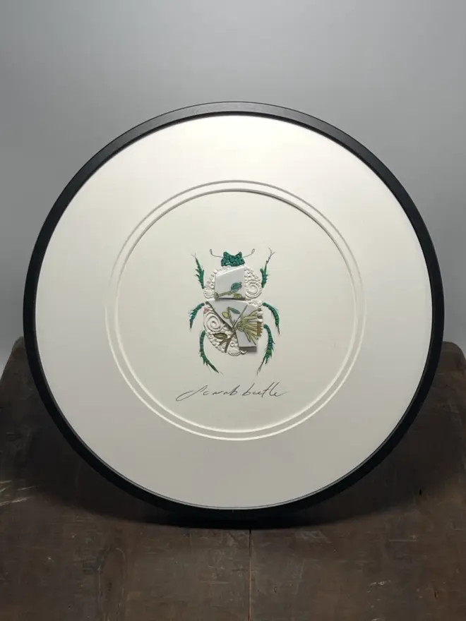 Hand-drawn, painted, mosaic clay, vintage yellow floral pottery insect on white double mounted card, in a black circular frame.