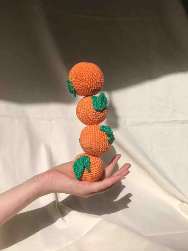 Stack of four crochet oranges balanced on a hand against a cloth background 