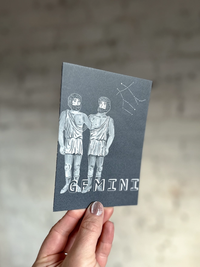a greetings card featuring a greyscale illustration of a zodiac style twins with the text “GEMINI”