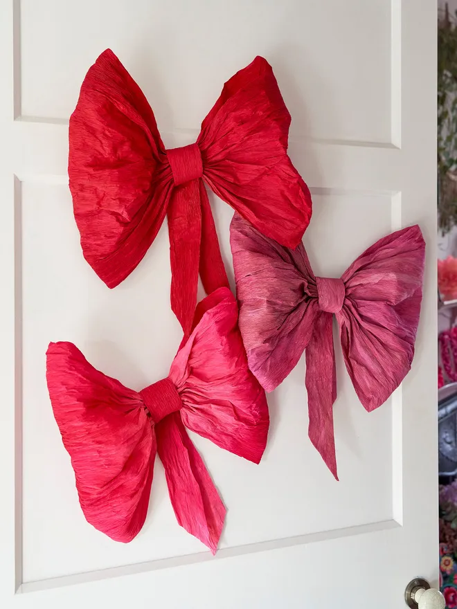 Large crepe paper pink and red bows. Three large paper bows hung on a white door