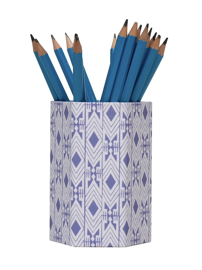 Tijan Hexagonal Brush Pot, a colourful patterned pencil pot sitting on a white surface against a plain backdrop. It is filled by some pencils. 