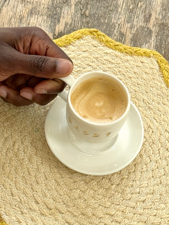 Espresso cup and saucer with DADDY emlazoned on the side with gold lustre detailing being lifted by a hand