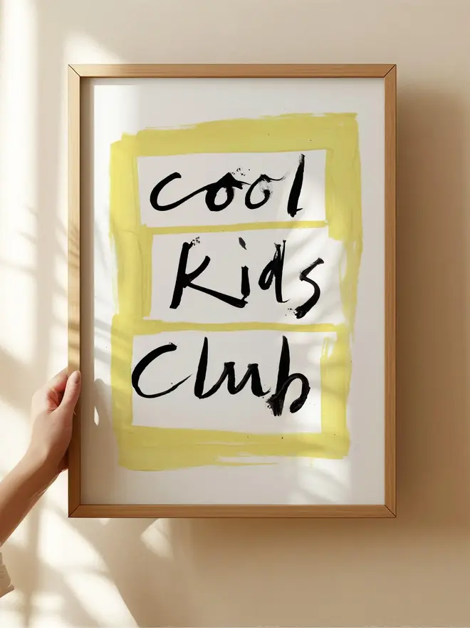 'cool kids club' art print. a print with a white and yellow background with a slogan in black lettering, framed on a wall.