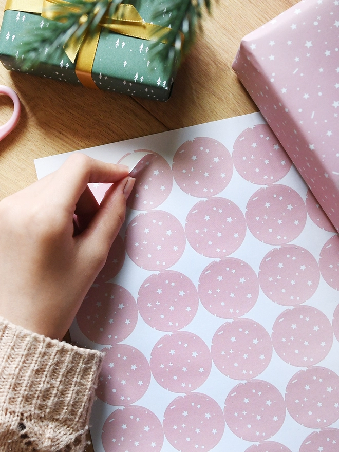 A hand is peeling a round sticker with a pink and white star design from a sheet of 35 stickers.