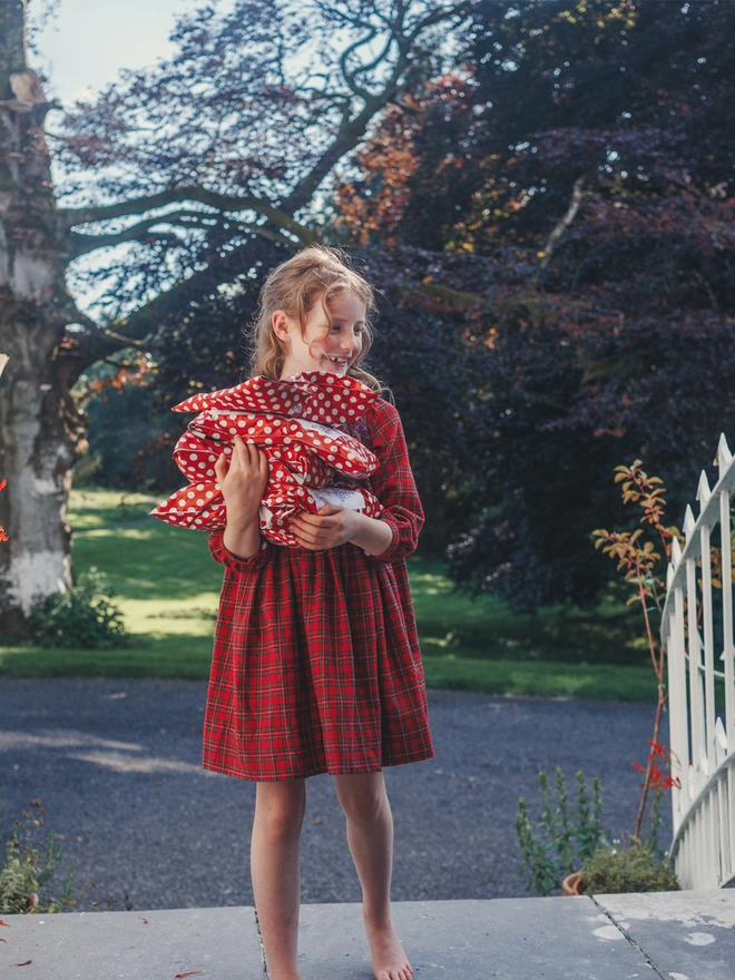 A girl stands holding parcels wearing a red tartan dress 