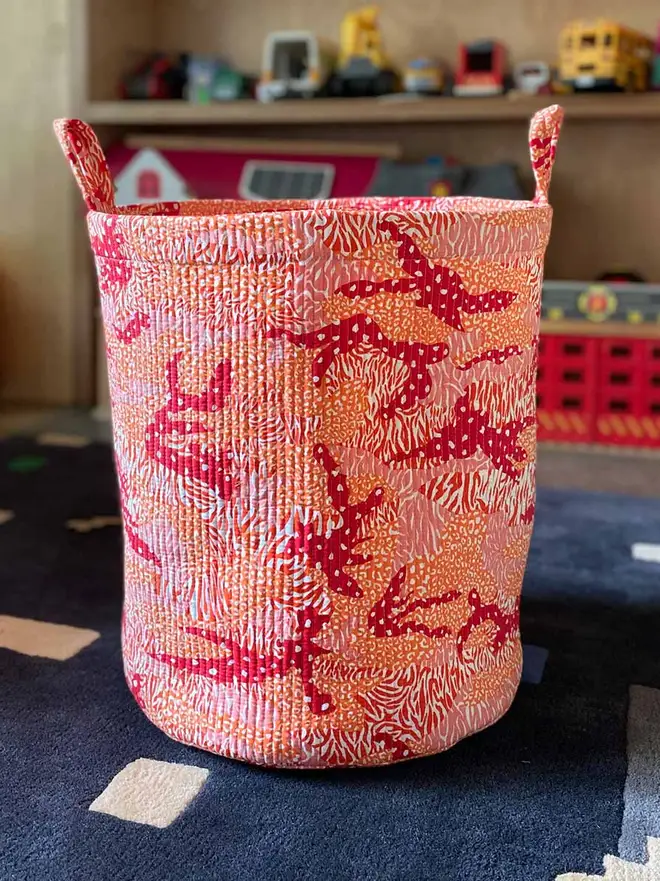 Orange Big Cat Camo Quilted Storage Basket, an orange storage basket sitting in a child's playroom. In the background can be seen more toys. 
