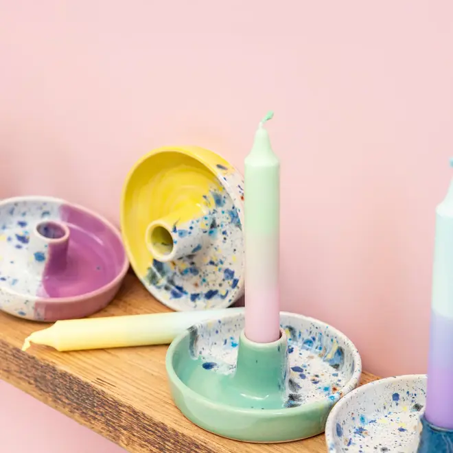 Shoreline Candle Stick Holder, a collection of colourful candle stick holders placed on a wooden shelf. They sit against a pink backdrop. 