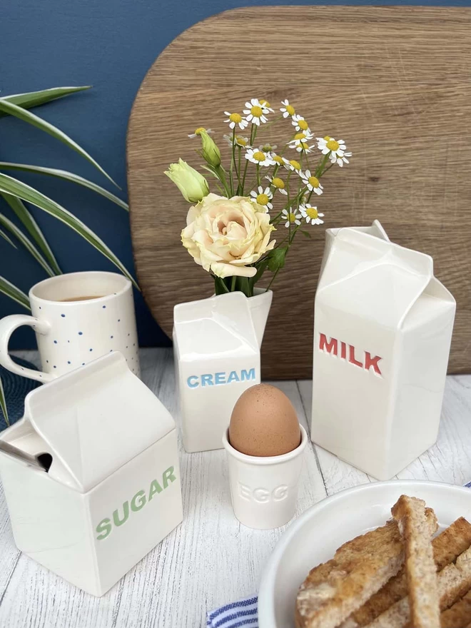 A handmade ceramic milk carton stands with matching sugar pot, butter dish and cream carton