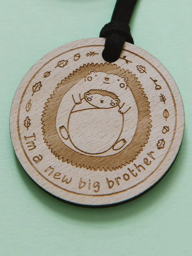 Wooden medal etched the the words "I'm a new big brother" underneath 2 sibling hedgehogs
