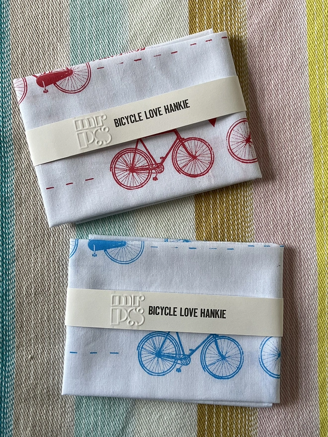 Two Mr.PS Bicycle Love printed cotton handkerchiesfs, folded and packaged, on a stripy tablecloth