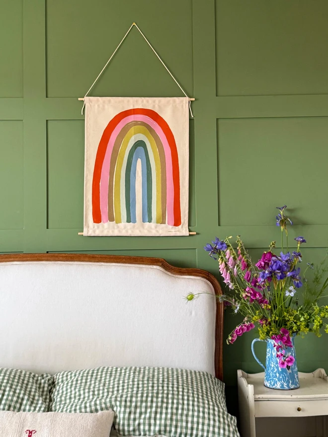Cotton Pastel Rainbow Fabric Banner, against a green wall. 