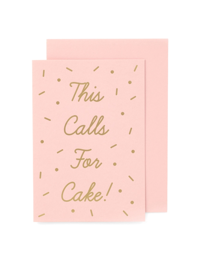 An elegant pink greeting card that says 'This Calls For Cake!', surrounded by Gold Sprinkles, with an envelope that has a seal