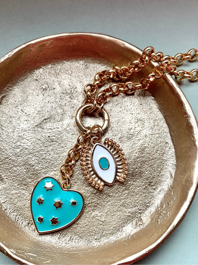 Gold chain necklace with a turquoise and gold star heart and a turquoise evil eye in a small gold dish