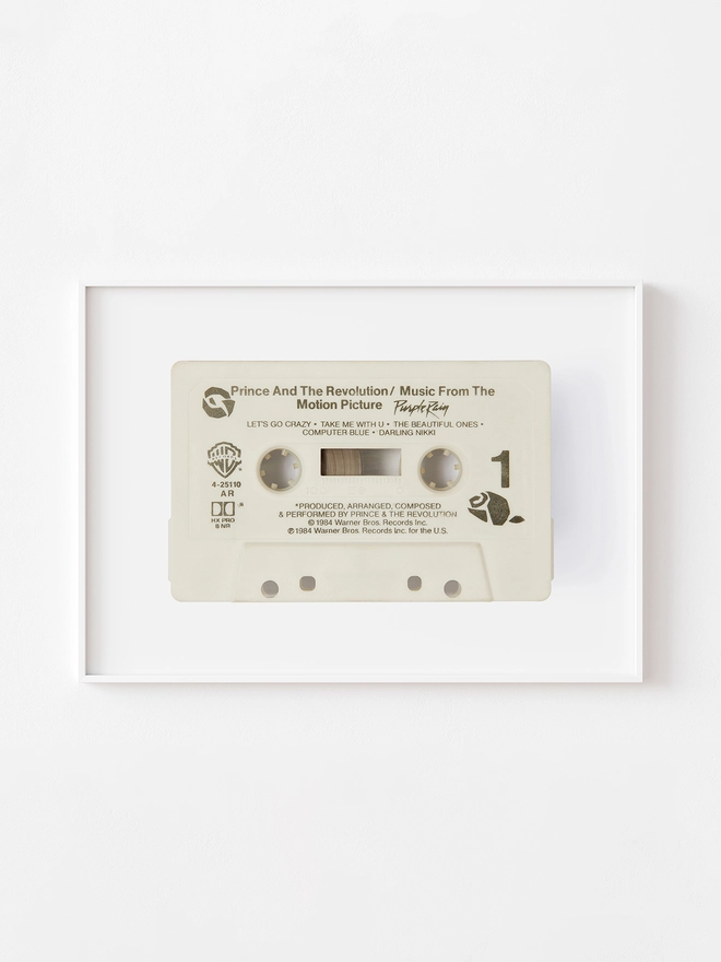 prince purple rain cassette tape print. framed print hung up on white wall.