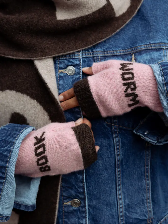 Lifestyle image of a person wearing the Calamine & Cocoa Book Worm Fingerless Mittens, with a denim jacket on