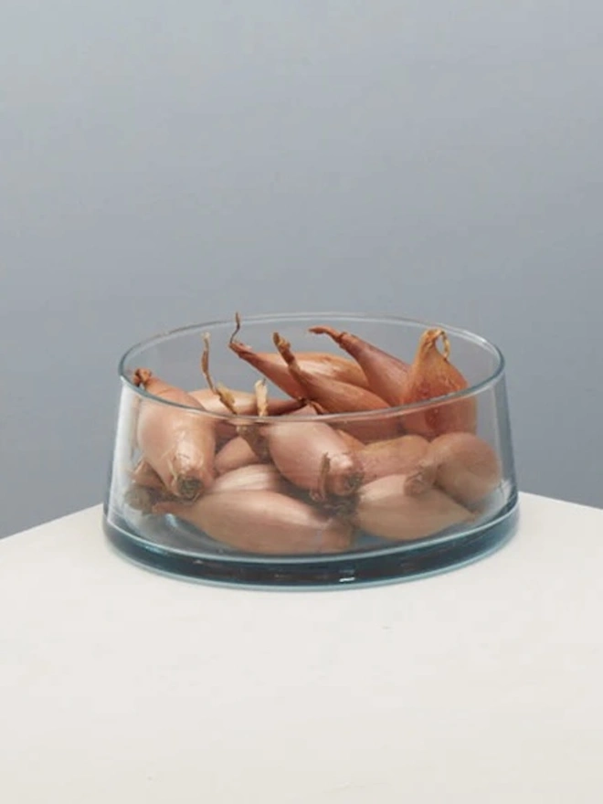 Low Glass Dish, a small glass dish sitting on a white counter top against a baby blue backdrop. It is filled by some food. 