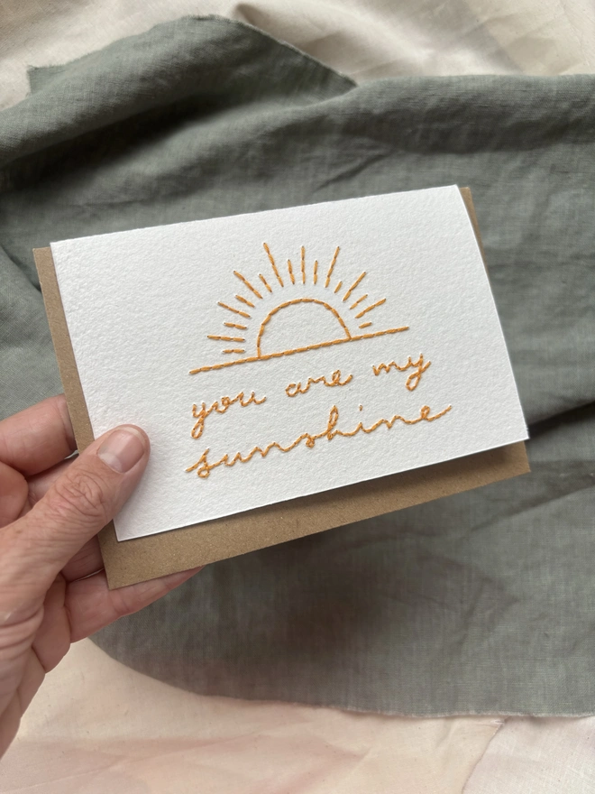 You are my sunshine hand embroidered card with yellow cursive lettering on a white background with Kraft envelope