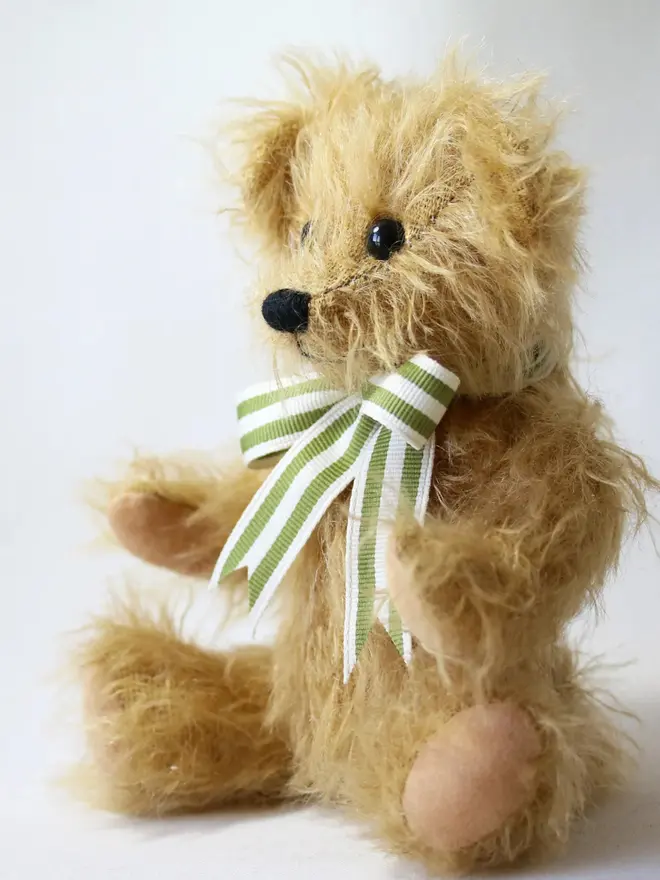 Handmade brown teddy bear sitting upright with a green striped ribbon bow against a plain background.
