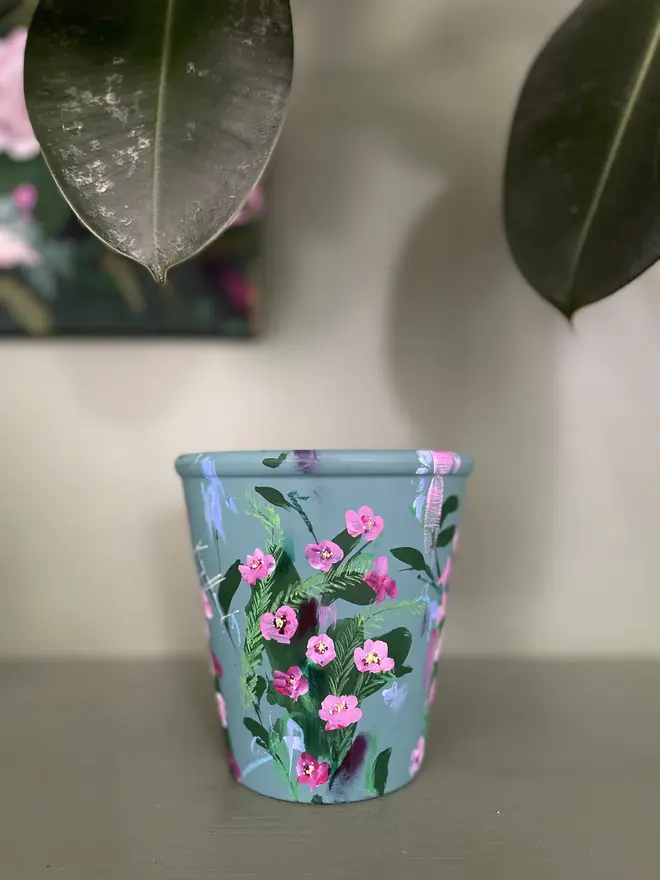 Hand painted terracotta floral plant pot dark sage background with vibrant pink wax flowers