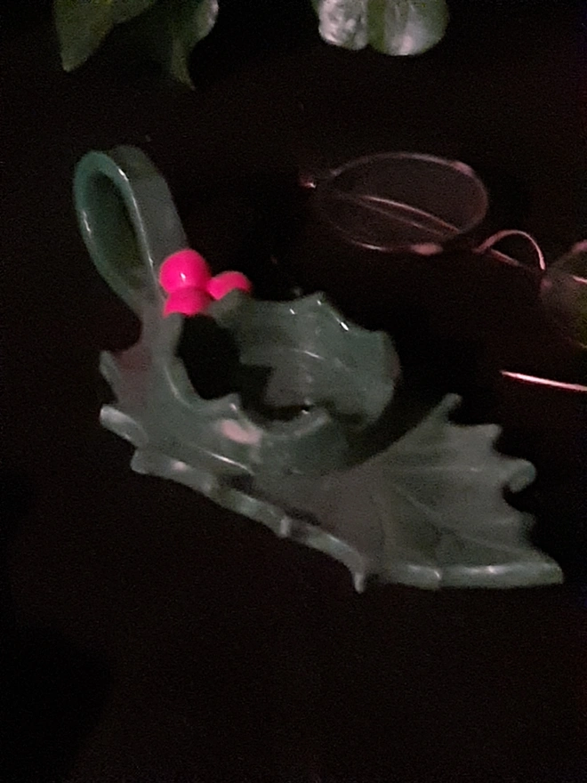 Handmade green ceramic holly leaf tealight holder with glossy red berries and loop handle, styled beneath trailing ivy.