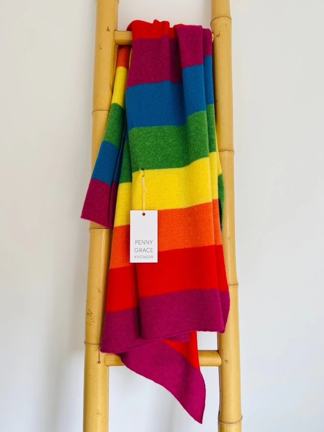 knitted rainbow blanket shown draped over a ladder