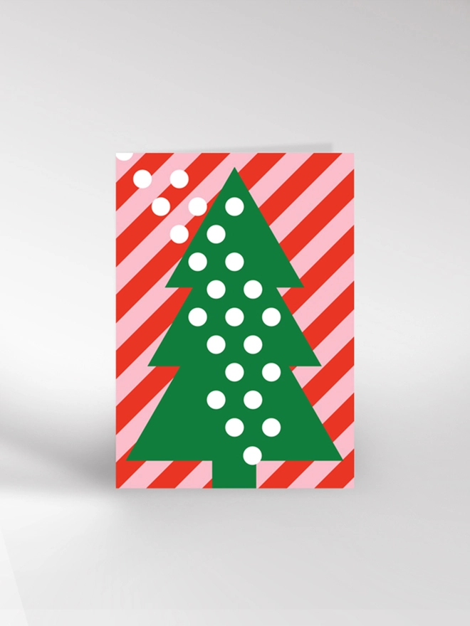 Contemporary illustrated card featuring a Christmas tree and falling snow on a striped background