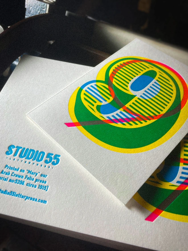 Detail of handmade letterpress 9th birthday card featuring bold overlapping numerals printed in vibrant fluorescent cyan, magenta and yellow inks. Each card is individually hand printed using traditional letterpress techniques on luxury paper stock, creating a beautifully tactile finish with a deep impression and rich layered colours inspired by the CMYK printing process. Printed on a traditional letterpress from 1915. A wonderful artisan printed birthday card.
