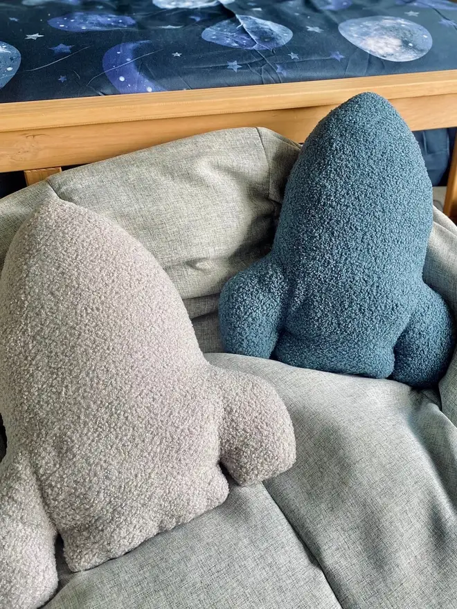 boucle rocket pillow. blue and grey rocket cushions on a bed with space-themed sheets.