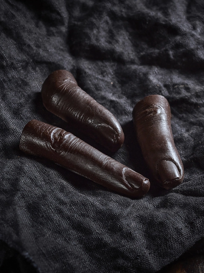 Realistic dark chocolate human fingers on dark cloth background
