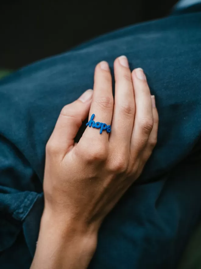 'Hope' Ring Original in blue seen on a hand.