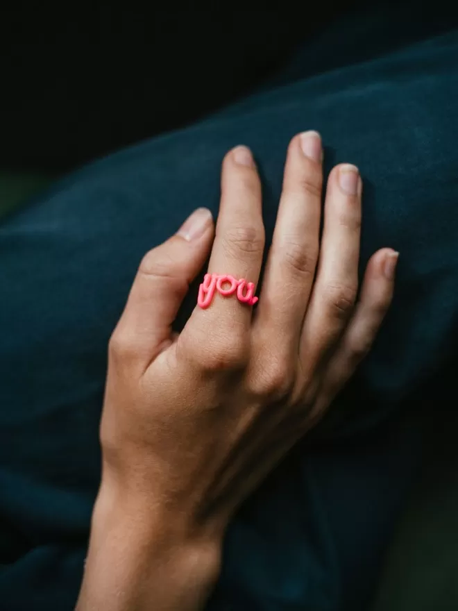 'You' Statement Reminder Ring in pink seen on a hand.