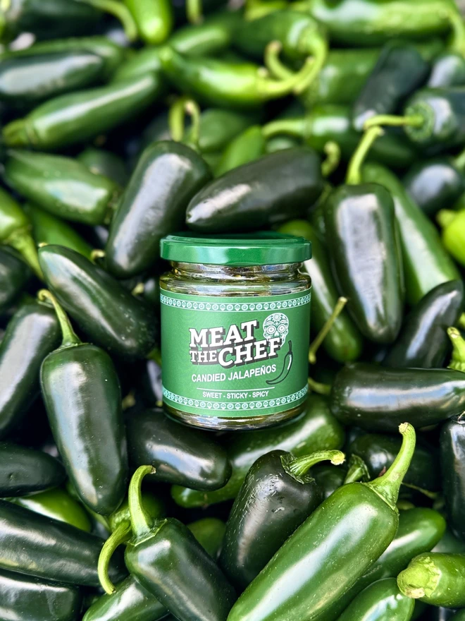 jar of candied jalapenos with a green label, nestled in a pile of bright green fresh jalapenos
