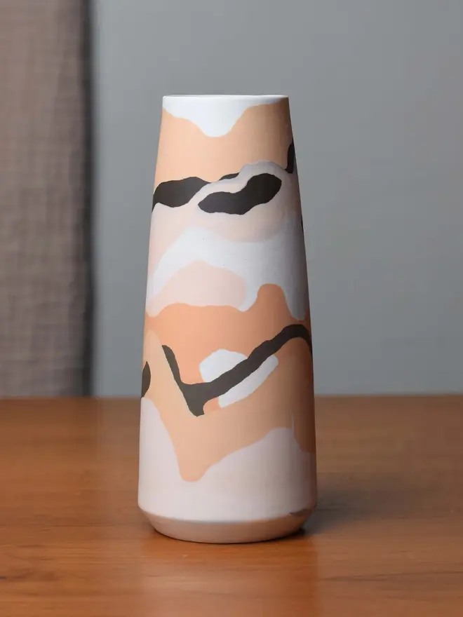 porcelain vase on table, vase has shades of orange, brown, and whites