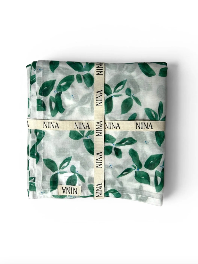 Emerald Leaves Muslin. A muslin patterned with green leaves, folded.