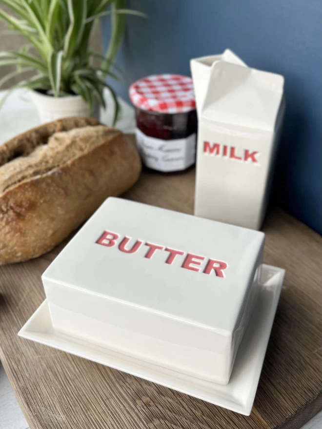 Handmade ceramic dish has butter painted in red on the lid, stands with matching milk carton.