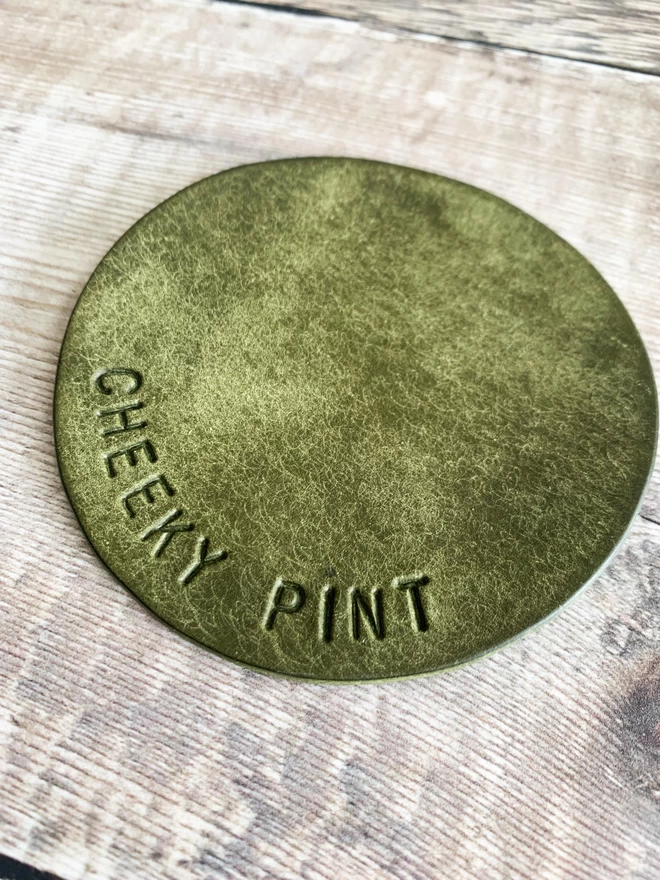Olive green leather coaster with 'cheeky pink' stamped on it.