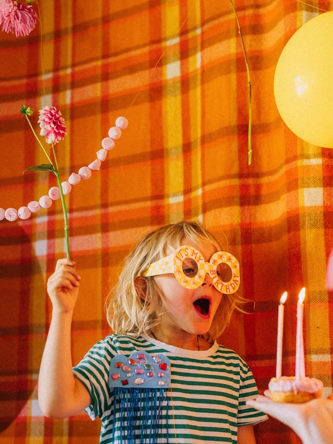 child wearing yellow and white grid card in shape of glasses with red birthday text