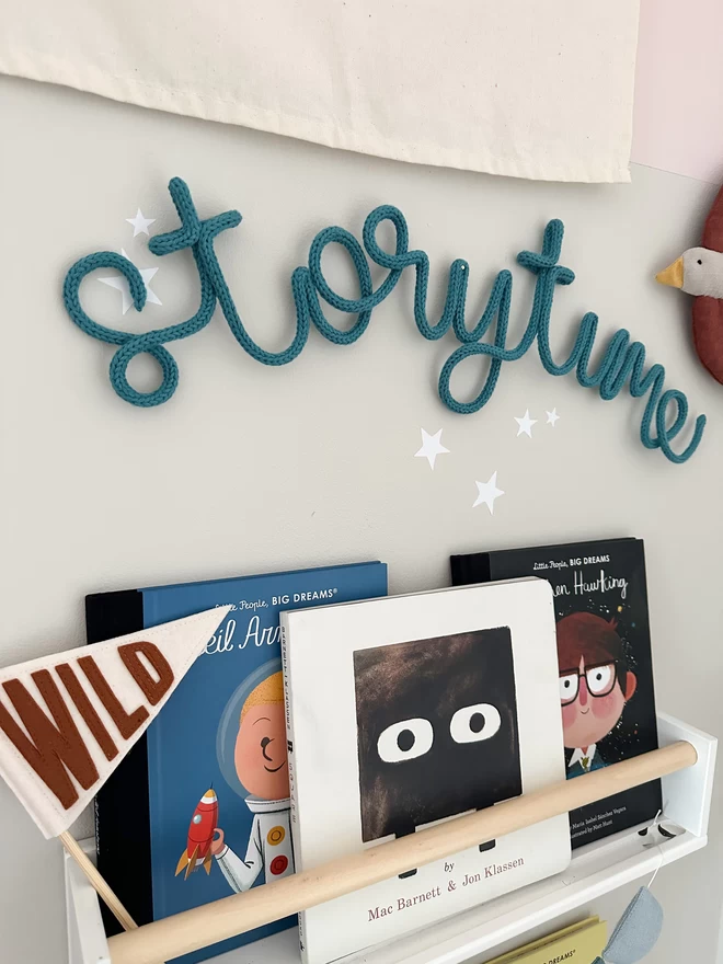 "storytime" knitted wall sign to hanging over child's book shelves filled with lots of books. 