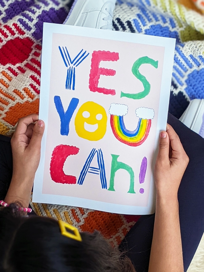 Young girl sitting holding an art print saying 'Yes you can'