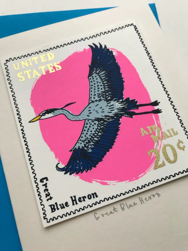 Bird Stamp Card Great Blue Heron/ American, a white card with a colourful bird design in the centre against a blue envelope on a white surface. 