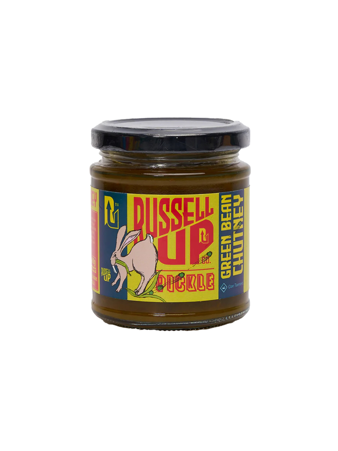 green bean chutney. a jar of green bean chutney photographed against a white background, featuring a rabbit eating green beans on the label.